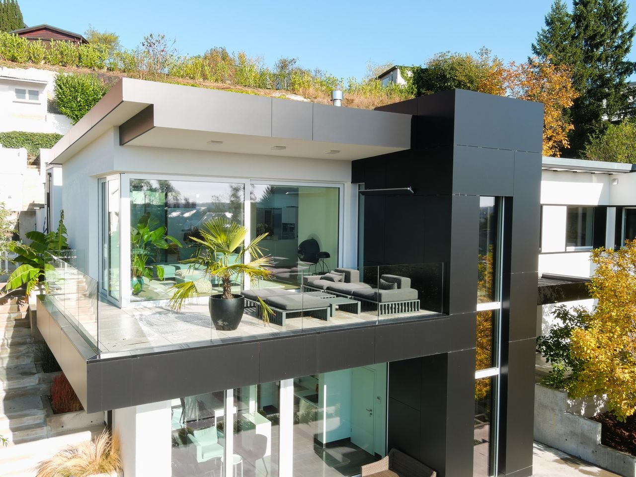 portfolio-02 Contemporary house featuring glass balcony, lush plants, and stylish design.