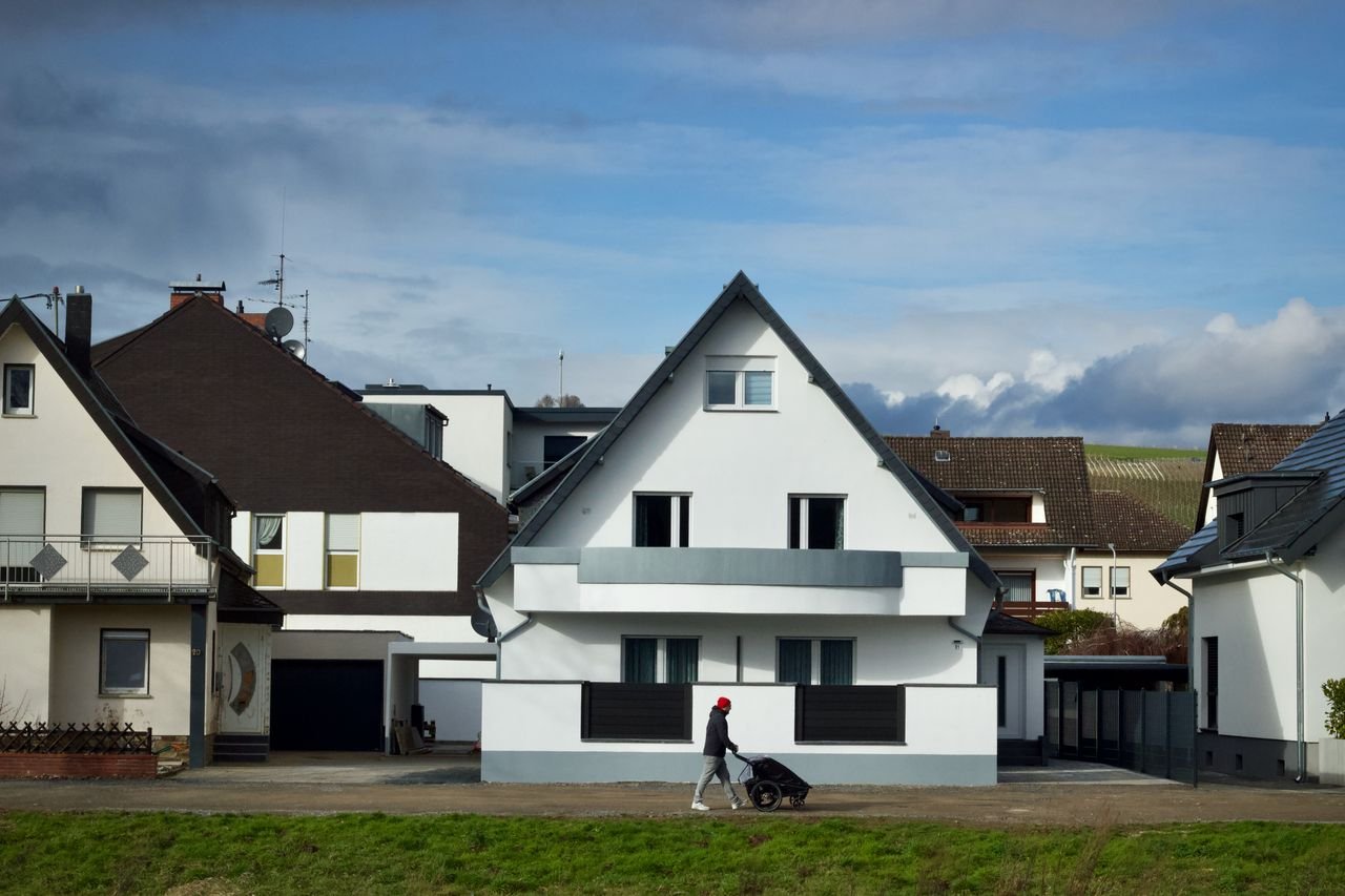 stats-img A person with a stroller walks by contemporary suburban houses under a bright sky.